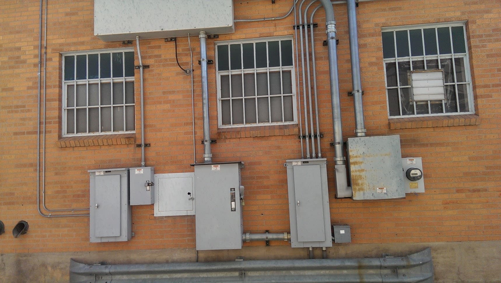 Brick building exterior with several electrical panels, a meter and conduit runs